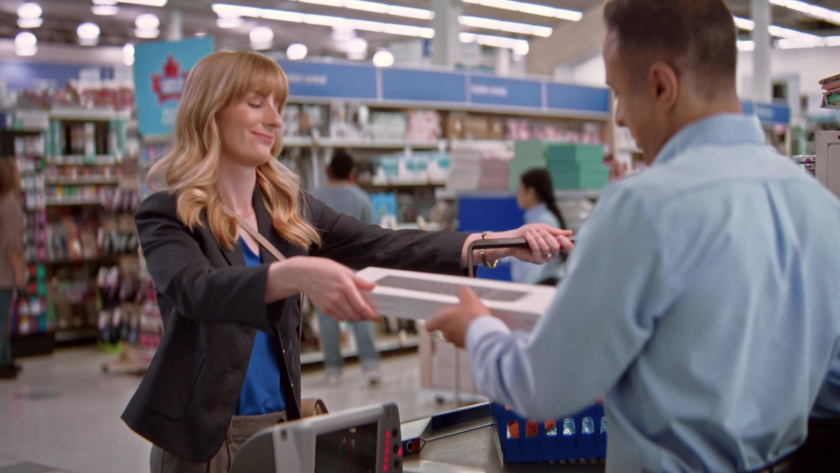 A customer hands a boxed electronic item to the cashier while smiling.