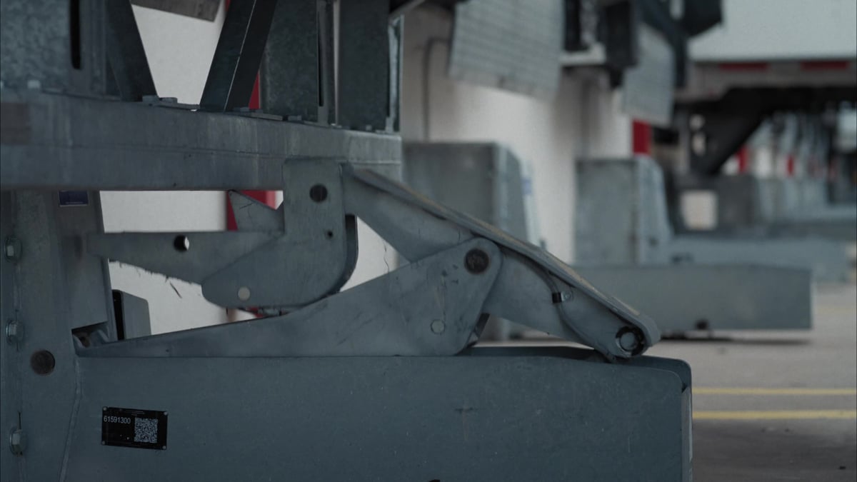 A close-up of heavy-duty trailer landing gear with a QR code asset tag