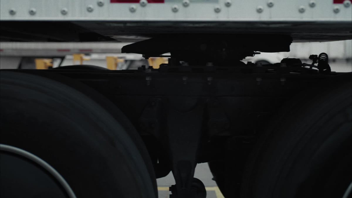 A ground-level view of a semi-trucks undercarriage, suspension, and dual rear tires