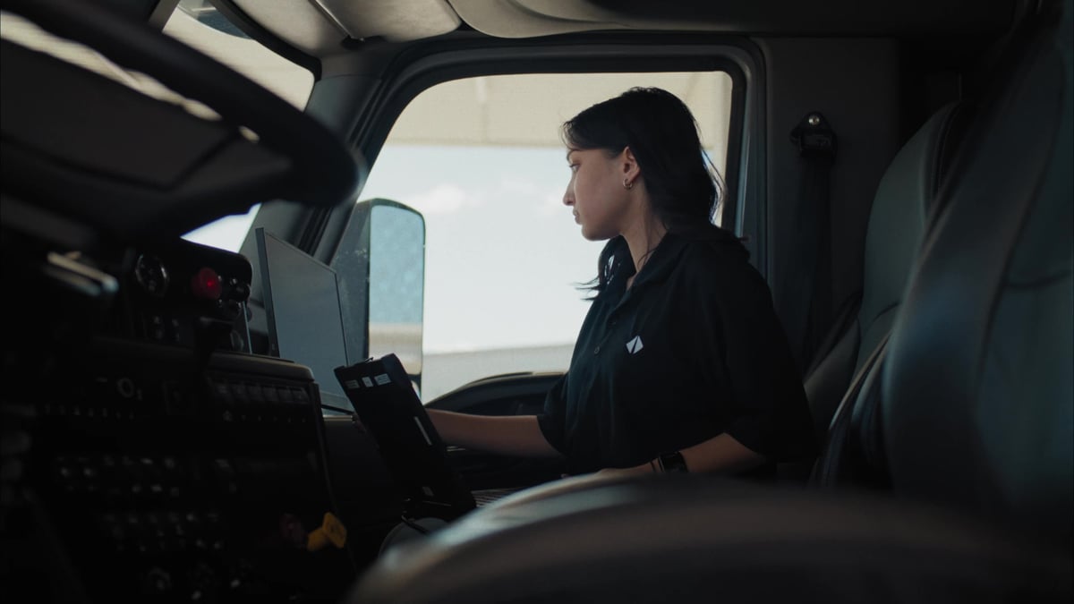 A woman in a black uniform reviews a tablet inside the cab of a semi-truck