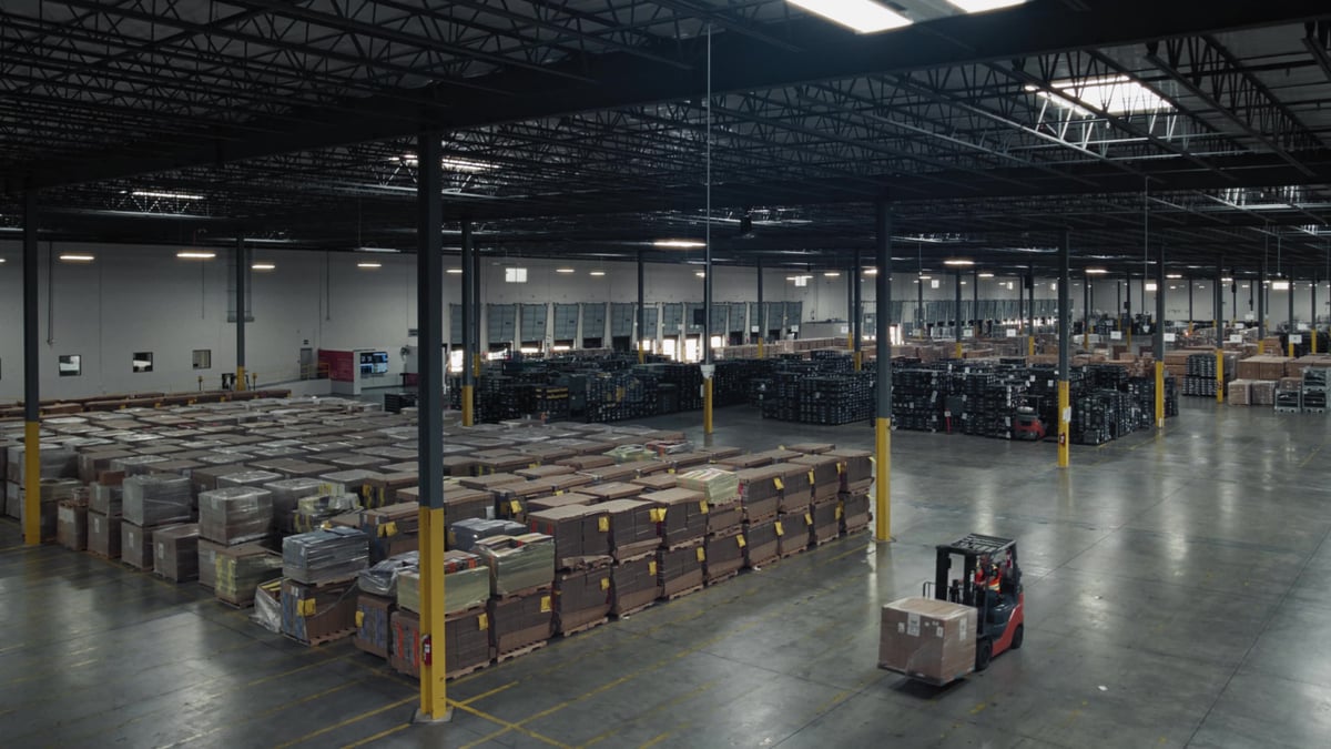 An aerial view of a large warehouse filled with palletized goods and a forklift in operation