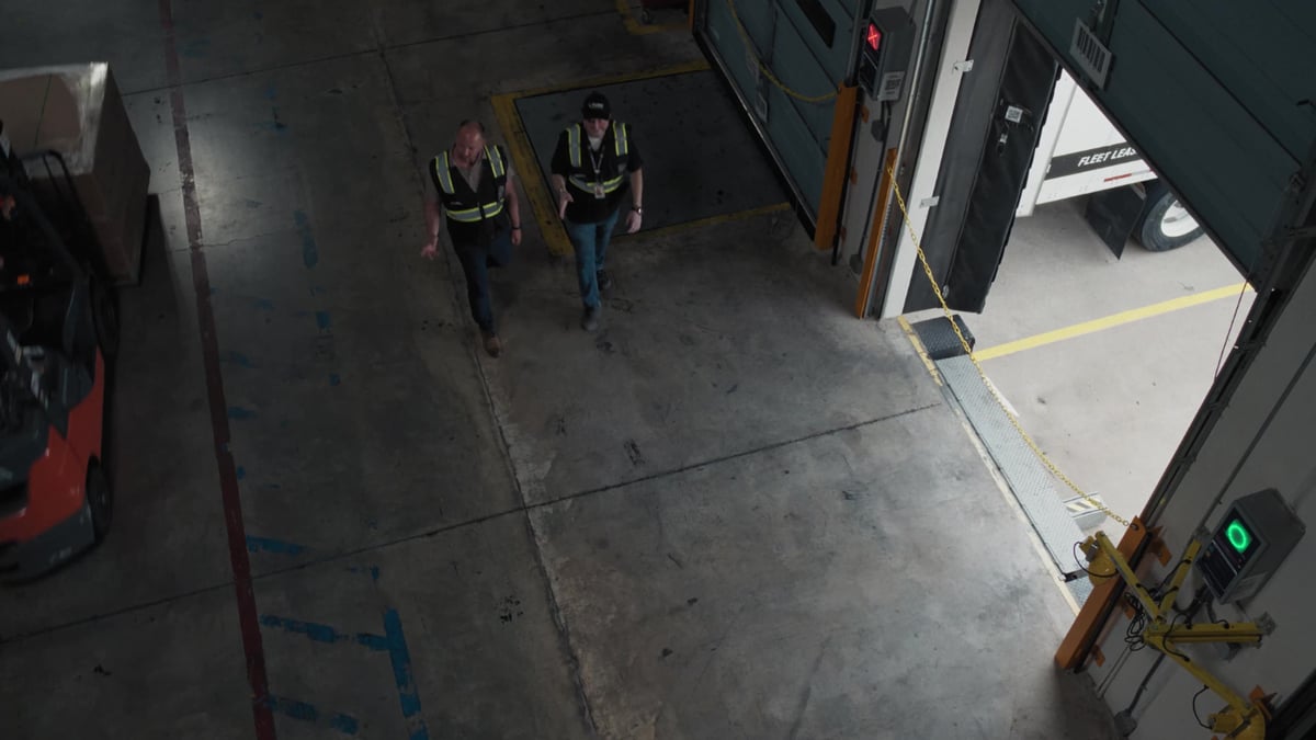 Two workers in high-visibility vests walk through a warehouse loading dock area