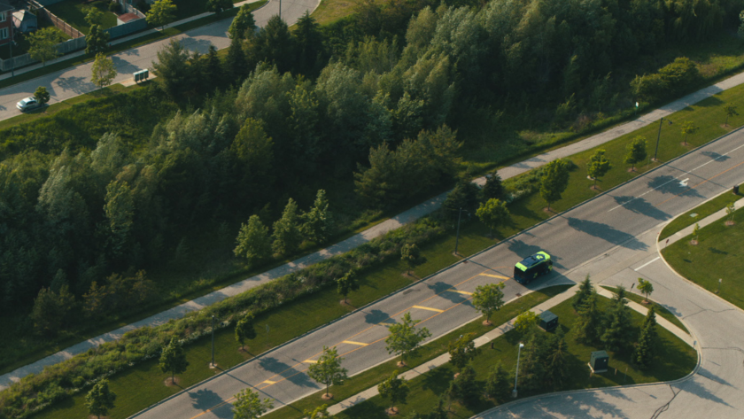 Aerial shot of a green and blue transit bus driving down a tree-lined suburban street.