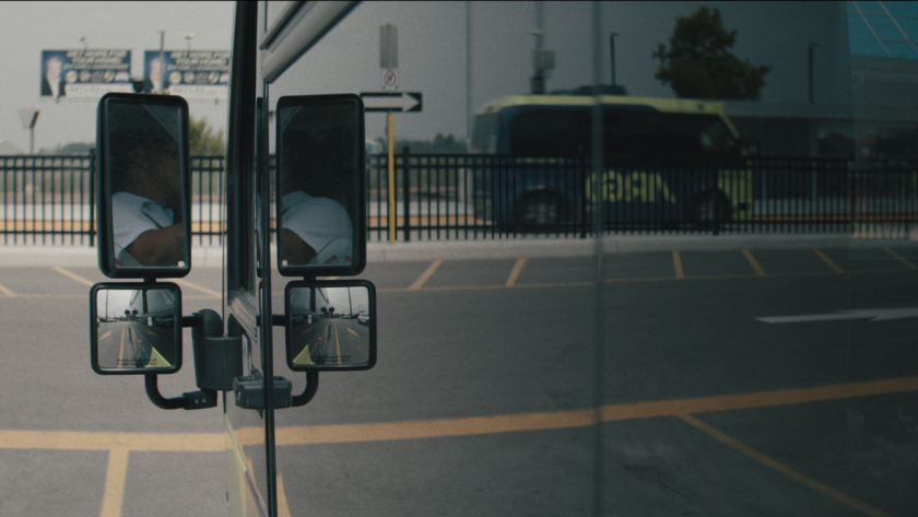 Reflections of a driver in the bus mirrors with another bus passing in the background.