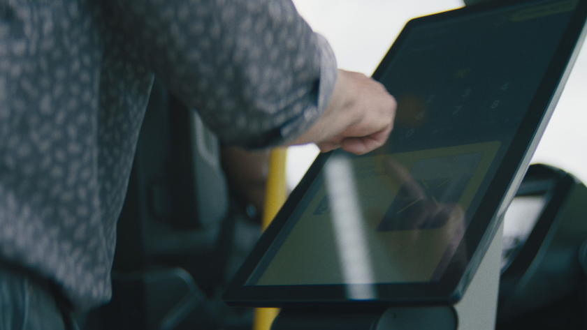 A passenger uses a touchscreen fare payment system inside the bus.
