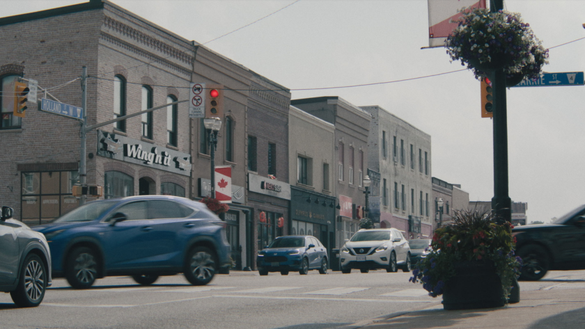 Street view of a busy small-town main street with cars, shops, and a traffic light.