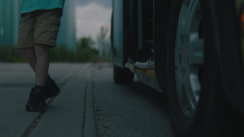 A child steps onto the curb near the bus with only their legs visible beside the wheel.