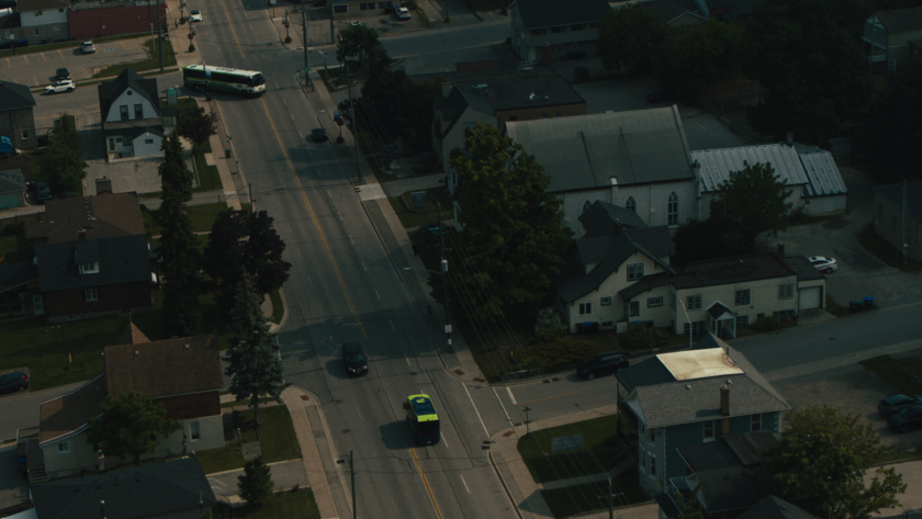 A Ride Argo bus moves down a small-town street lined with houses and trees.