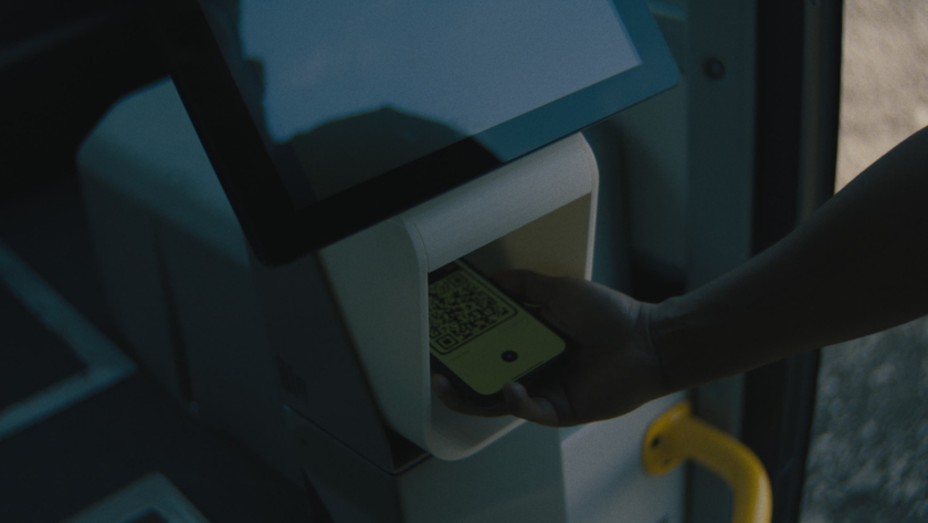 A rider scans a QR code ticket on a digital fare reader inside the bus.