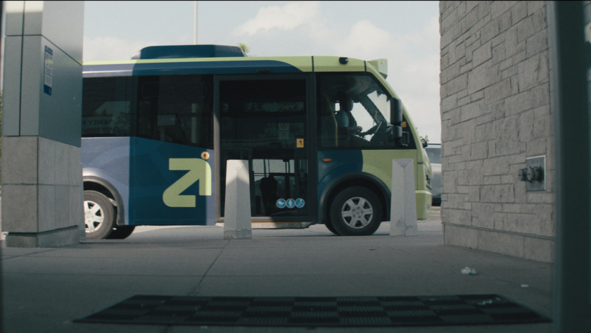A side view of the branded transit bus parked outside a building entrance.