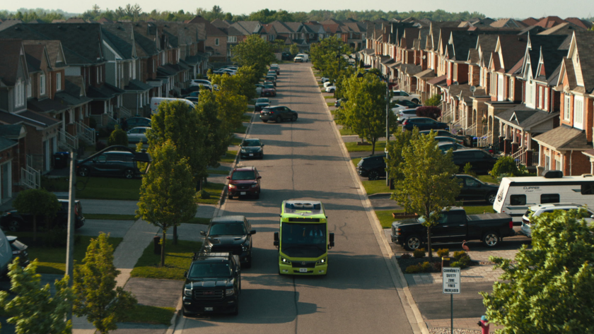 A Ride Argo shuttle bus drives down a suburban street lined with identical houses and parked cars.
