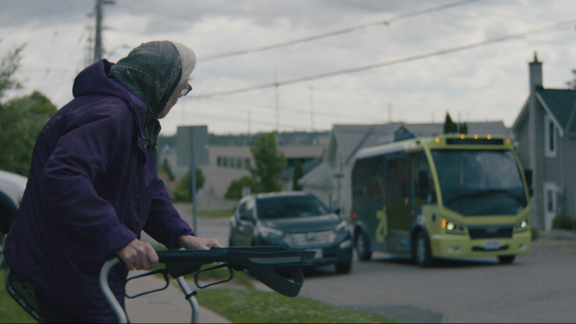 A person in a wheelchair looks toward a green and blue transit bus parked outside.