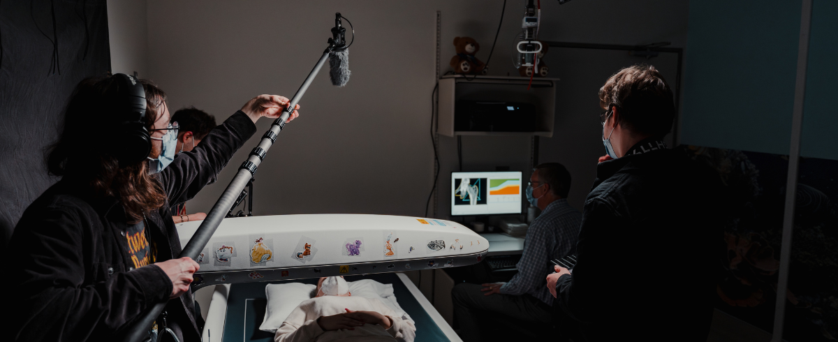 A crew holding a long microphone and a light for a specific scene where the leukemia patient is lying in bed.