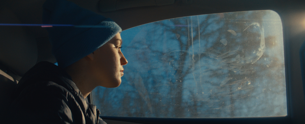 A young patient wearing a bonnet, looking outside the window of a car.