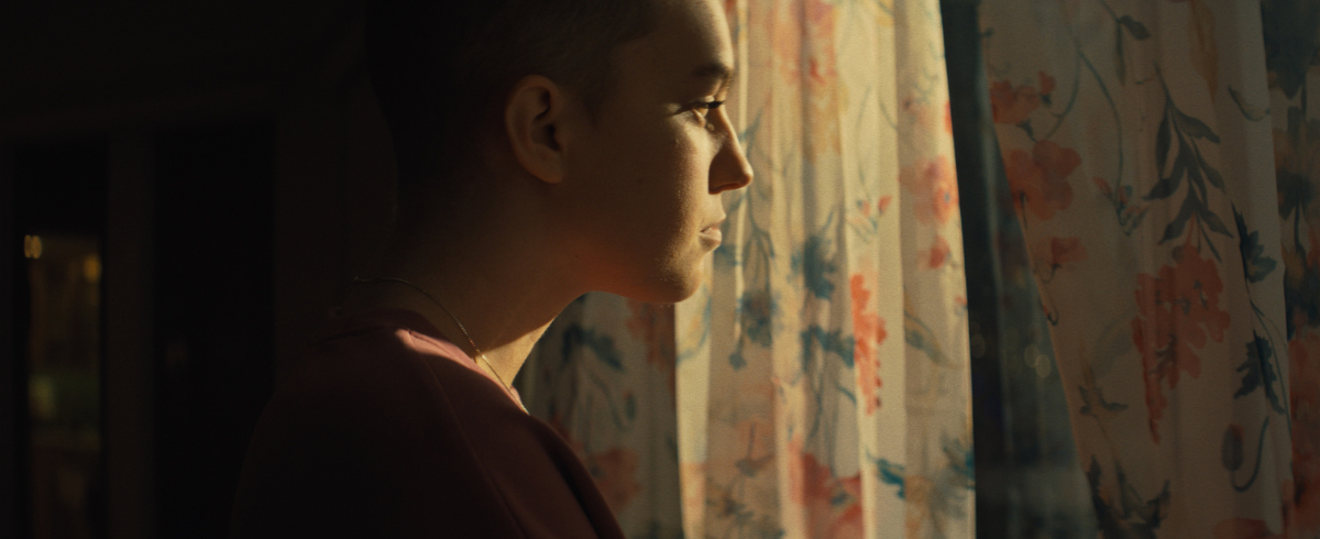 A leukemia patient looking outside the window of her house, with curtains, as light gently illuminates her.