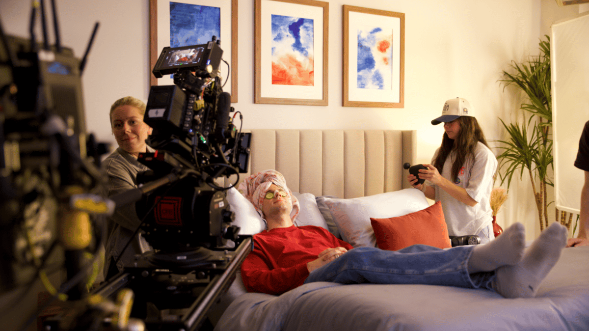 On the production set, the actor is being assisted with cucumbers on his eyes and a towel on his head, preparing for the shoot.
