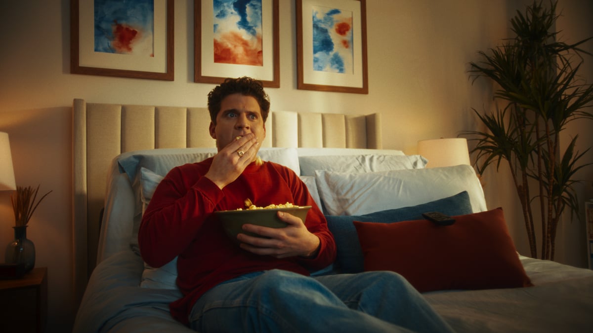 Man relaxing in bed while eating popcorn.