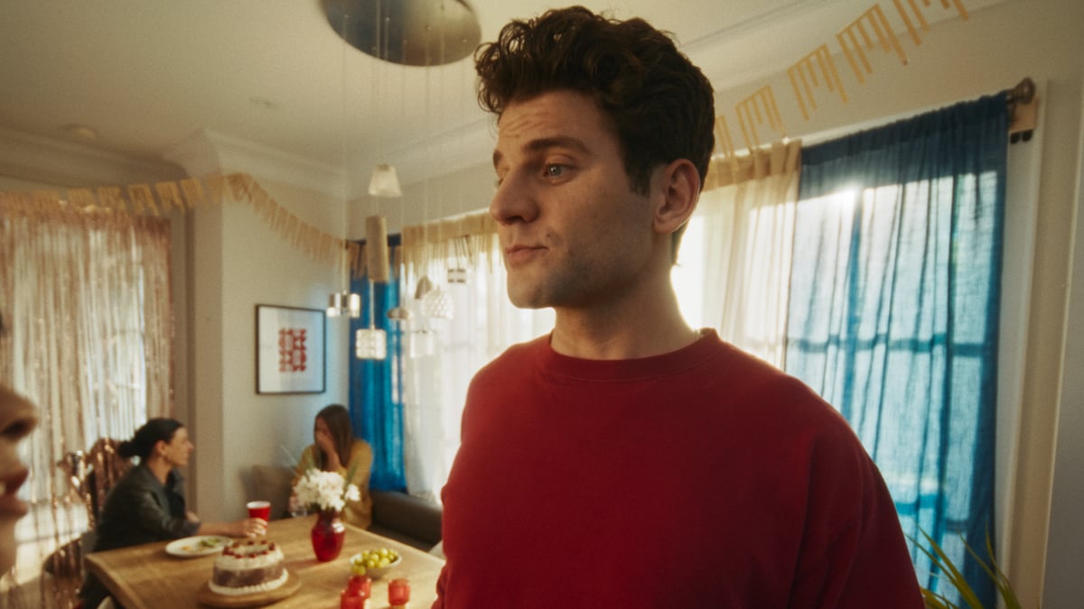 Man standing in a room where a party is happening, looking sleepy.
