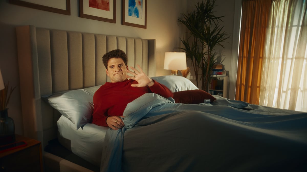 Man waking up and shyly waving to the people who opened the door.