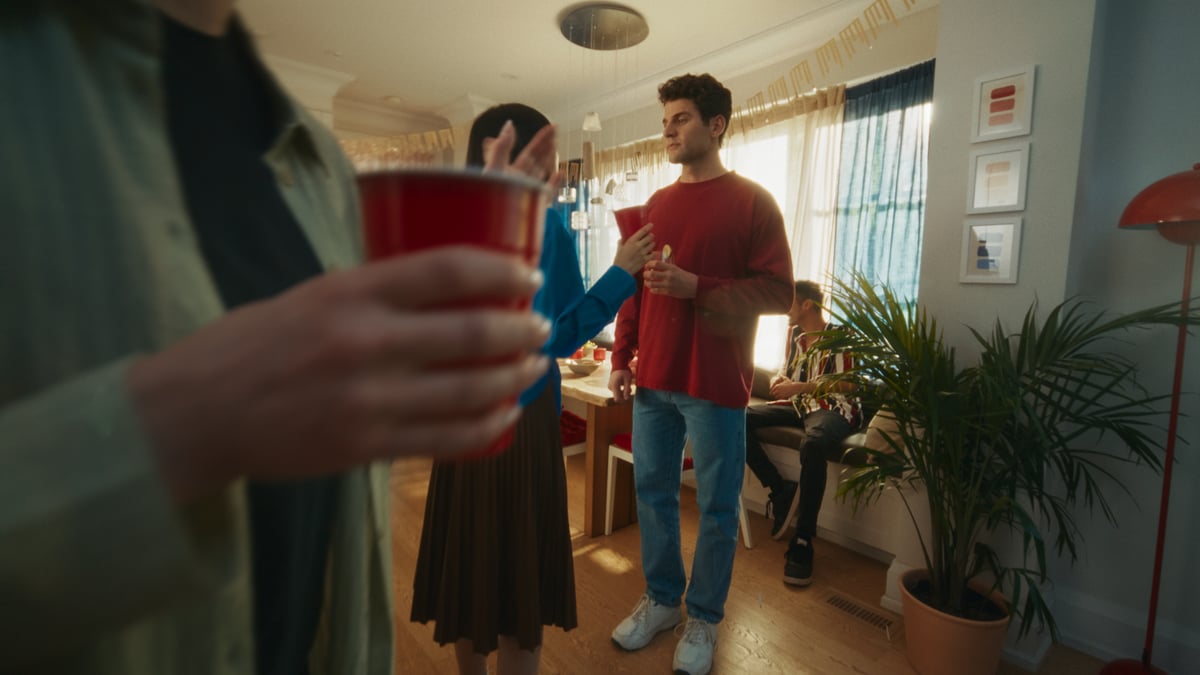 Man wearing a bright red pullover, talking to a woman at a party.