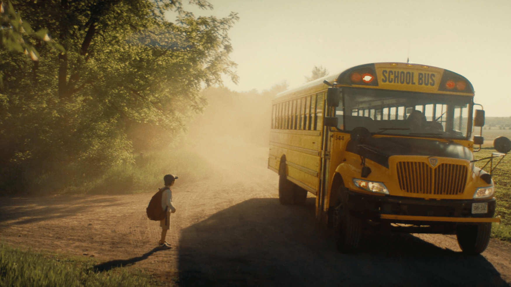 A young student runs toward an IC Bus school bus on a dusty rural road bathed in golden morning light, capturing the everyday moments of reliable school transportation.