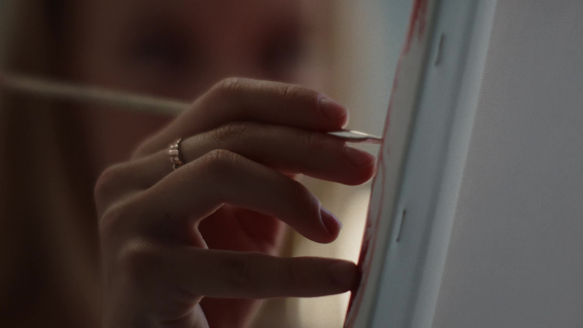 Close-up of a hand holding a paintbrush while working on a canvas.