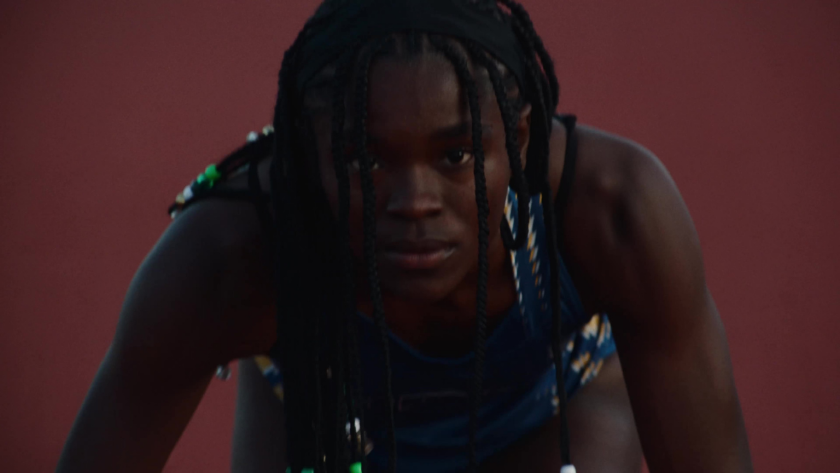 A focused athlete in starting position prepares to sprint on a red track.