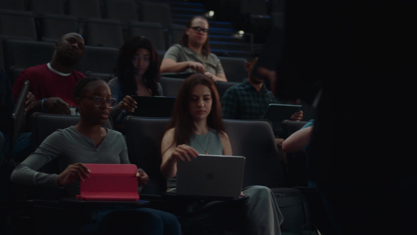 Students seated in a lecture hall prepare laptops and tablets during class.