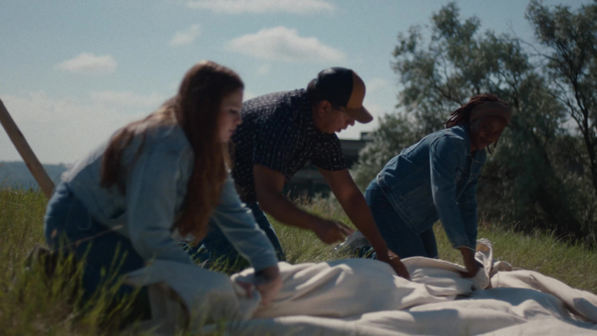 A group of students and a mentor work together to assemble a tipi covering on the grass.