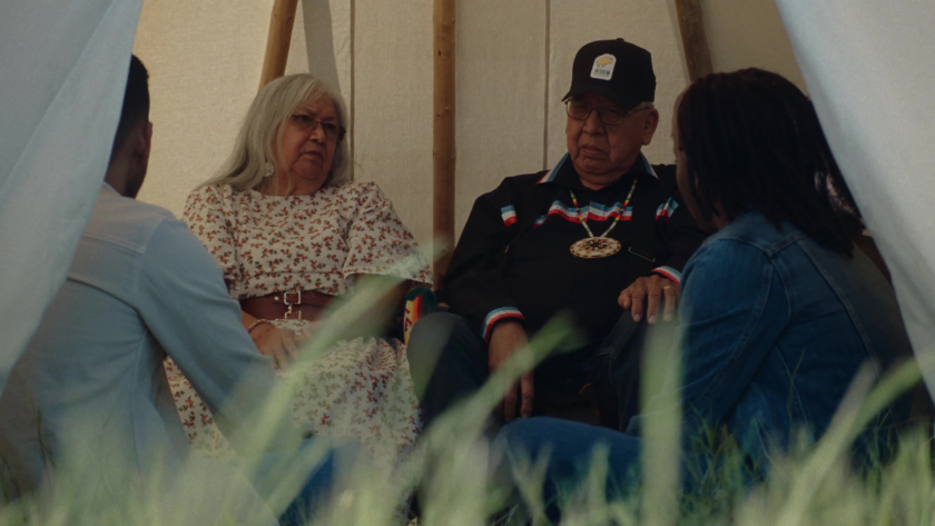 Elders and students sit together inside a tipi, engaged in conversation.