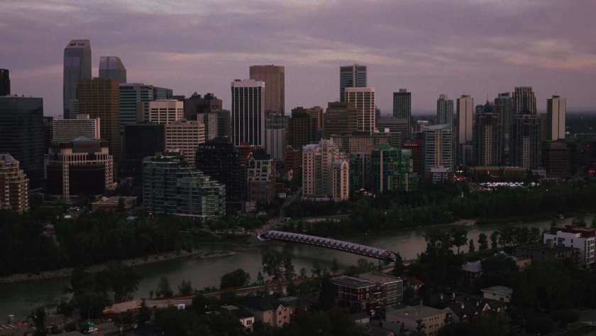 A wide view of Calgary’s downtown skyline at dusk with the Peace Bridge crossing the river in the foreground.