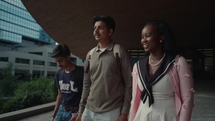 Three students walk together outside on campus, smiling and engaged in conversation.