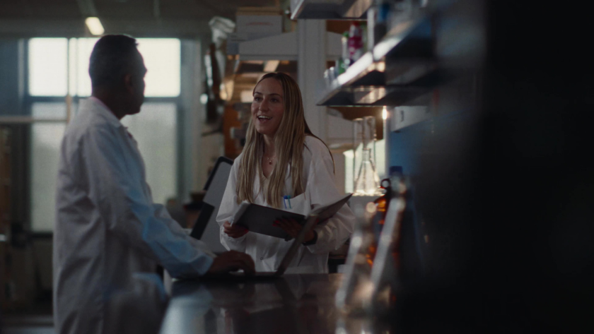Two researchers in lab coats converse while working in a bright laboratory.