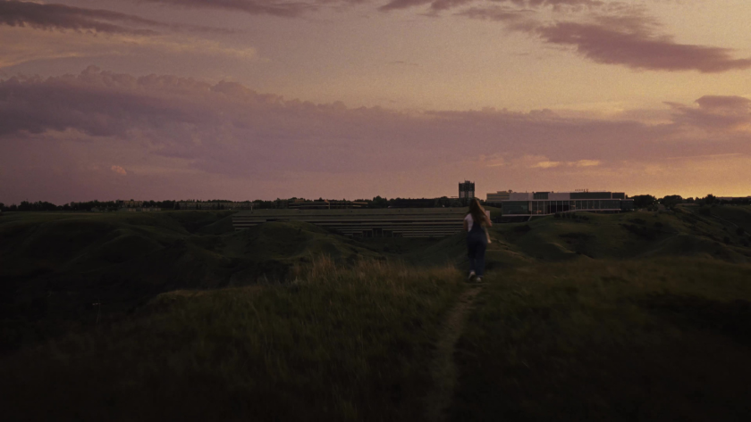 A student walks across a grassy hill at sunset with the University of Lethbridge in the distance.