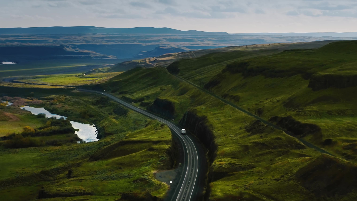 A lone vehicle navigates a winding highway through Iceland's dramatic green highlands, illustrating the freedom and adventure of automotive exploration in breathtaking natural landscapes.