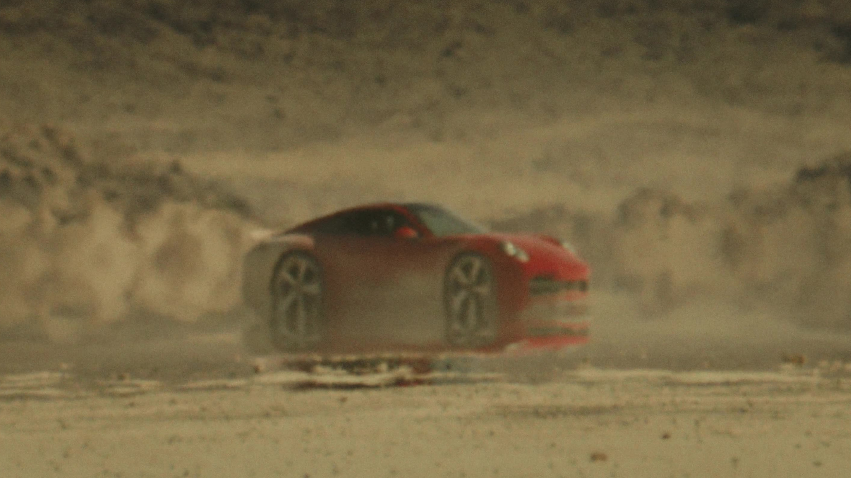Red Porsche 911 kicking up dust while drifting across the desert in the Porsche Mirage commercial