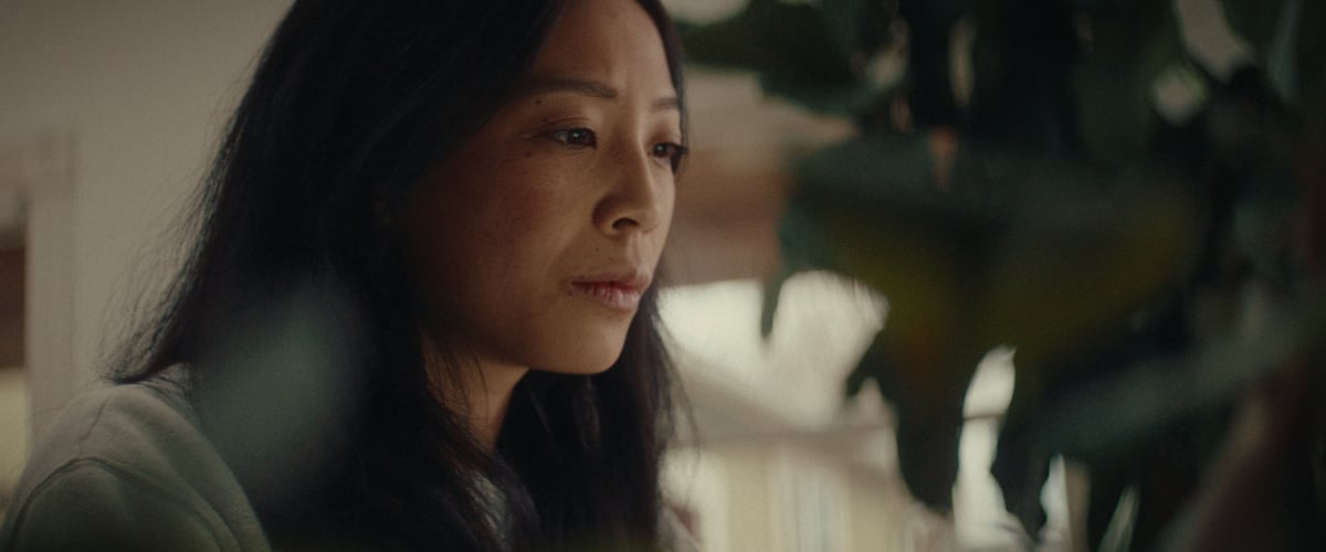 A woman, with a serious expression, gazes down at her computer while at home.