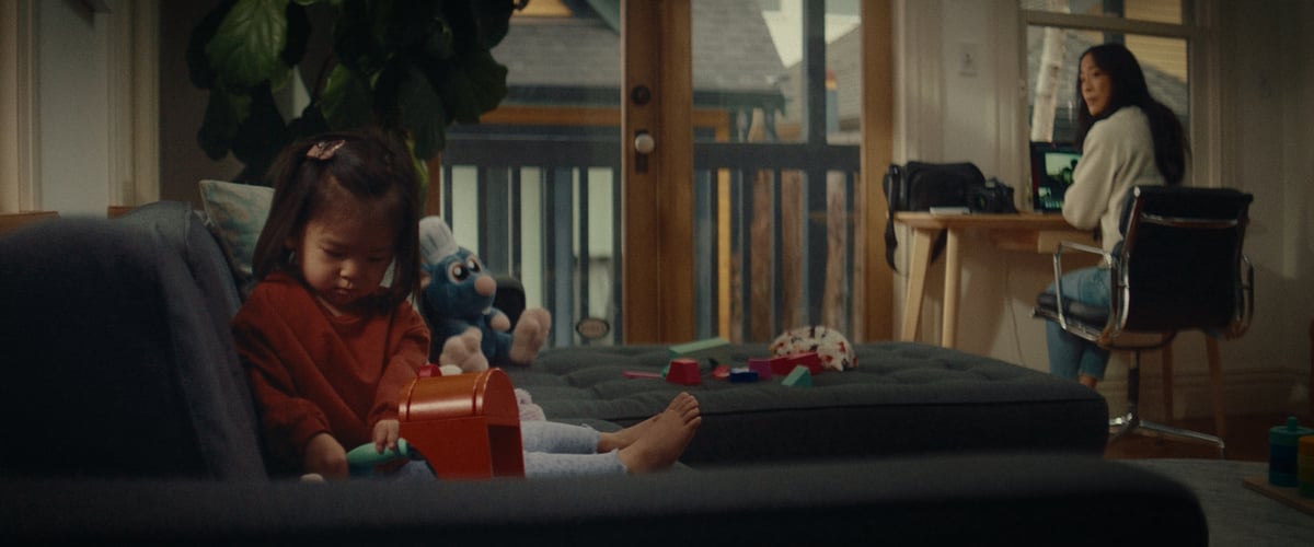 A woman seated at her computer desk turns around to watch her children playing on the couch.