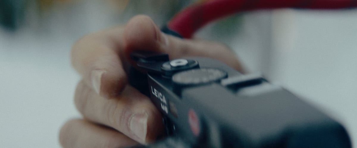 A hand holds a camera, with fingers poised over the shutter button, ready to click it.