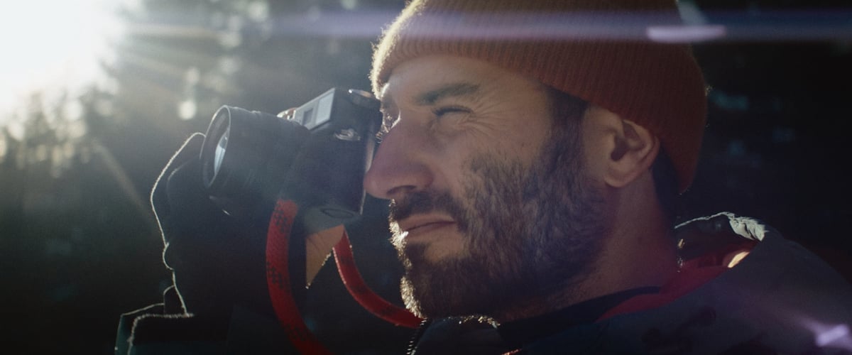 A man squints one eye while positioning the camera to his other eye, capturing a picture of a stunning view.