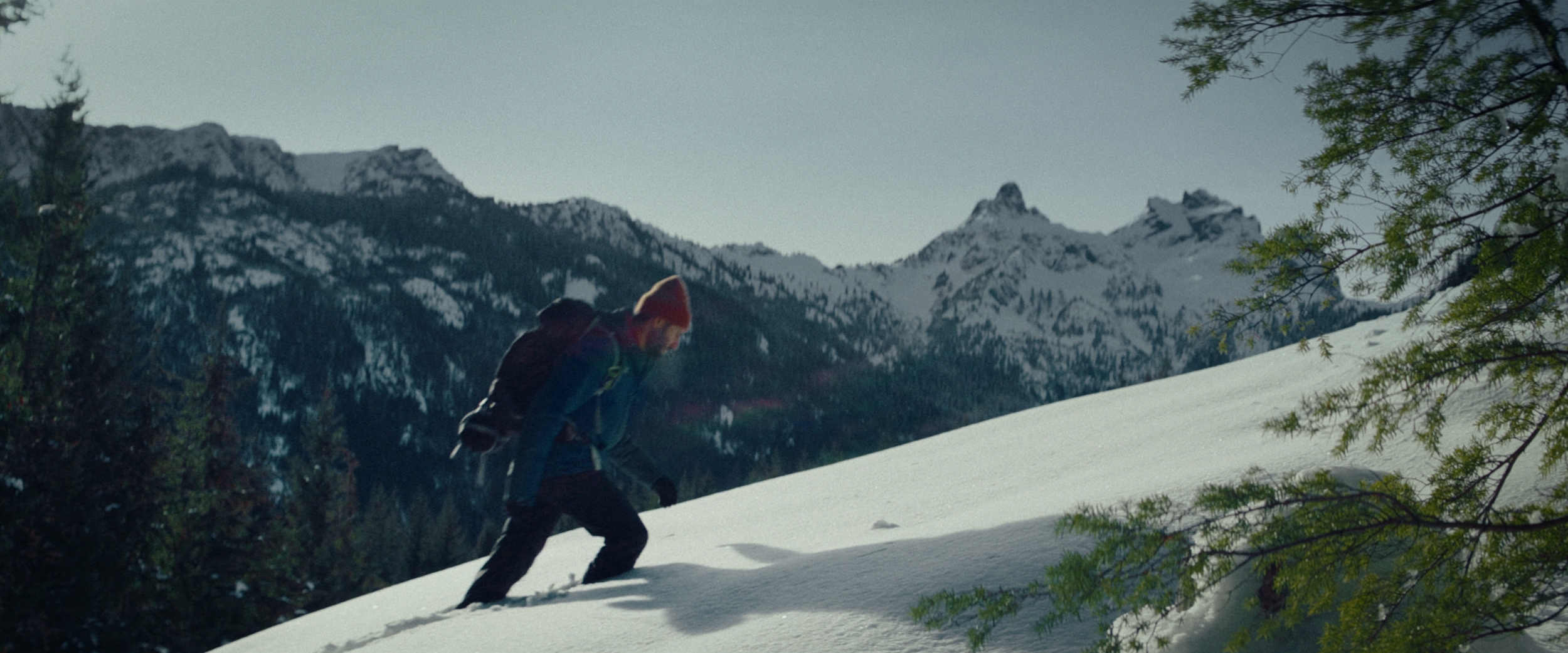 A man ascending a snow-covered mountain, with a breathtaking scenic backdrop.