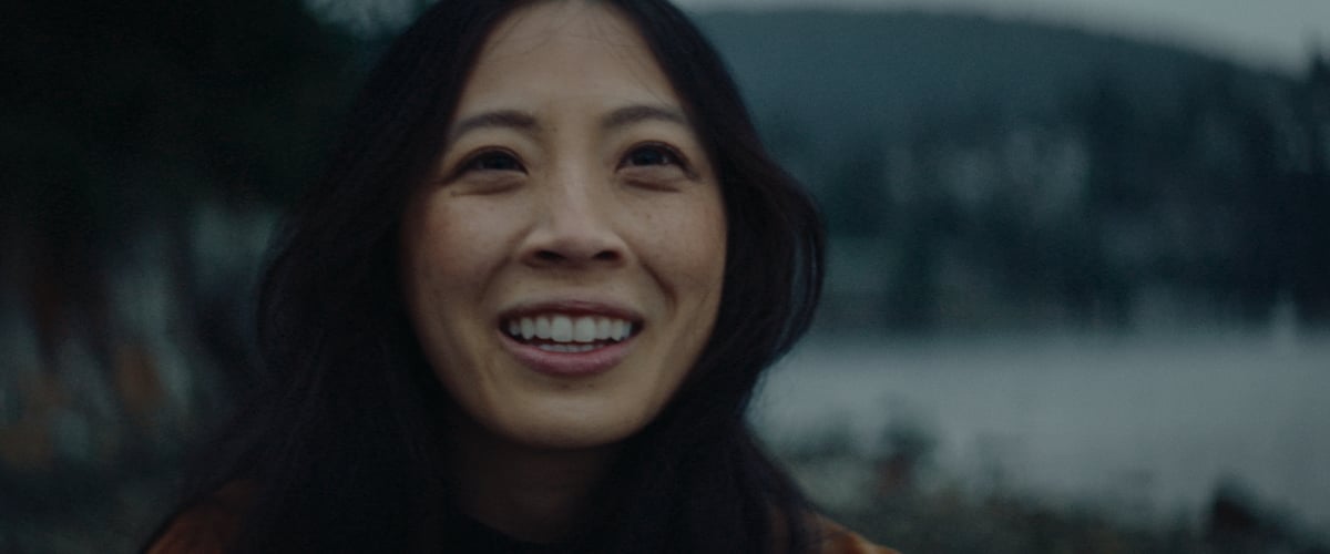An image capturing a close-up of a woman's smiling face by the lakeside.
