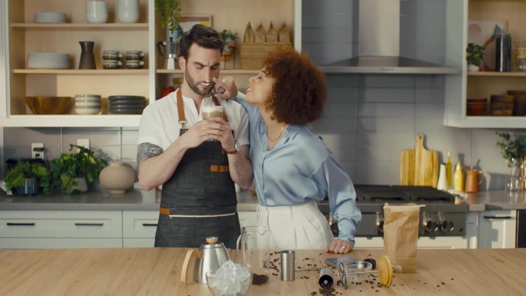 A couple cooks together at a bright kitchen counter, sharing a playful moment.