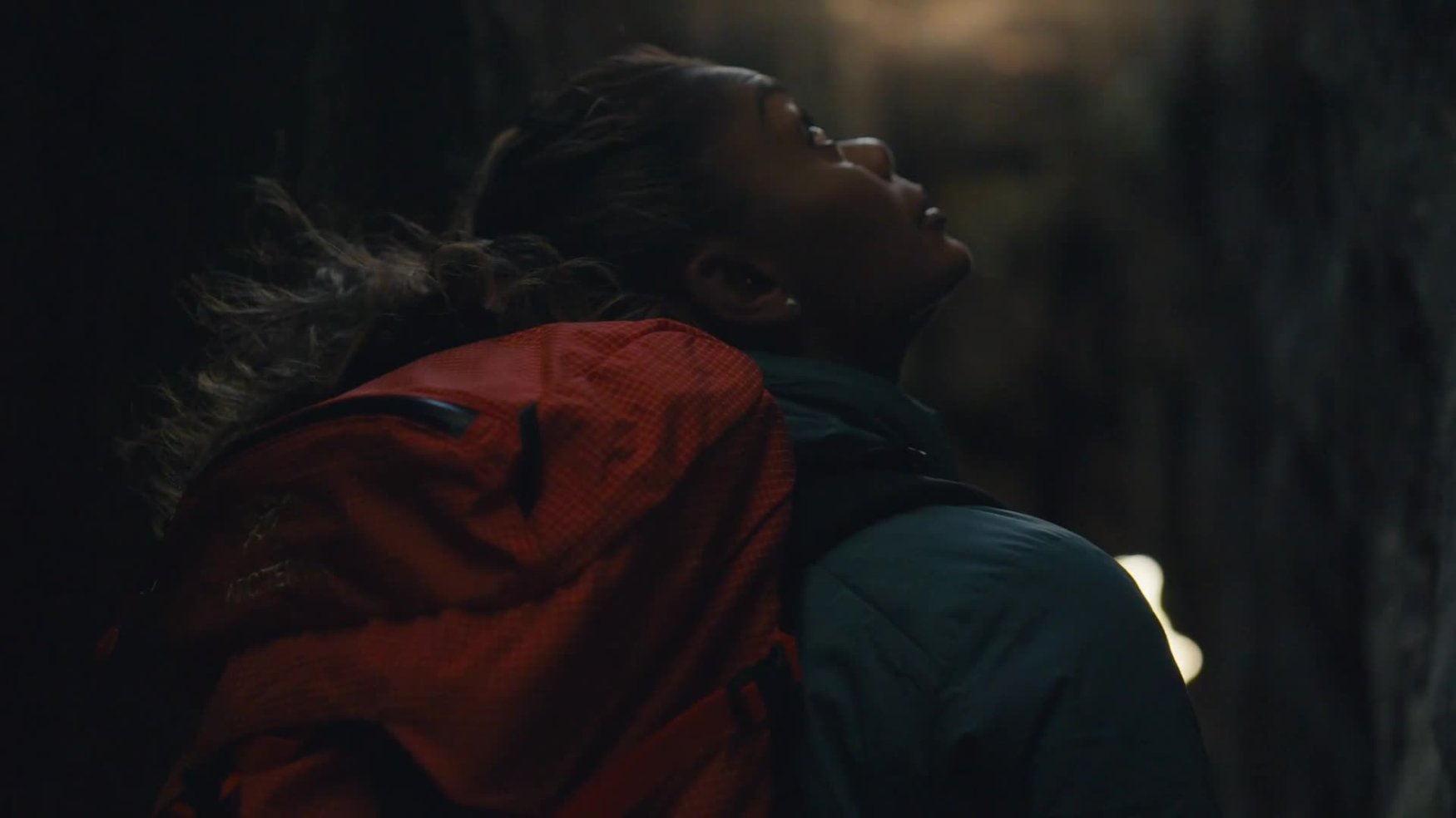 A woman in a red jacket embraces someone in a dramatic, dimly lit close-up.