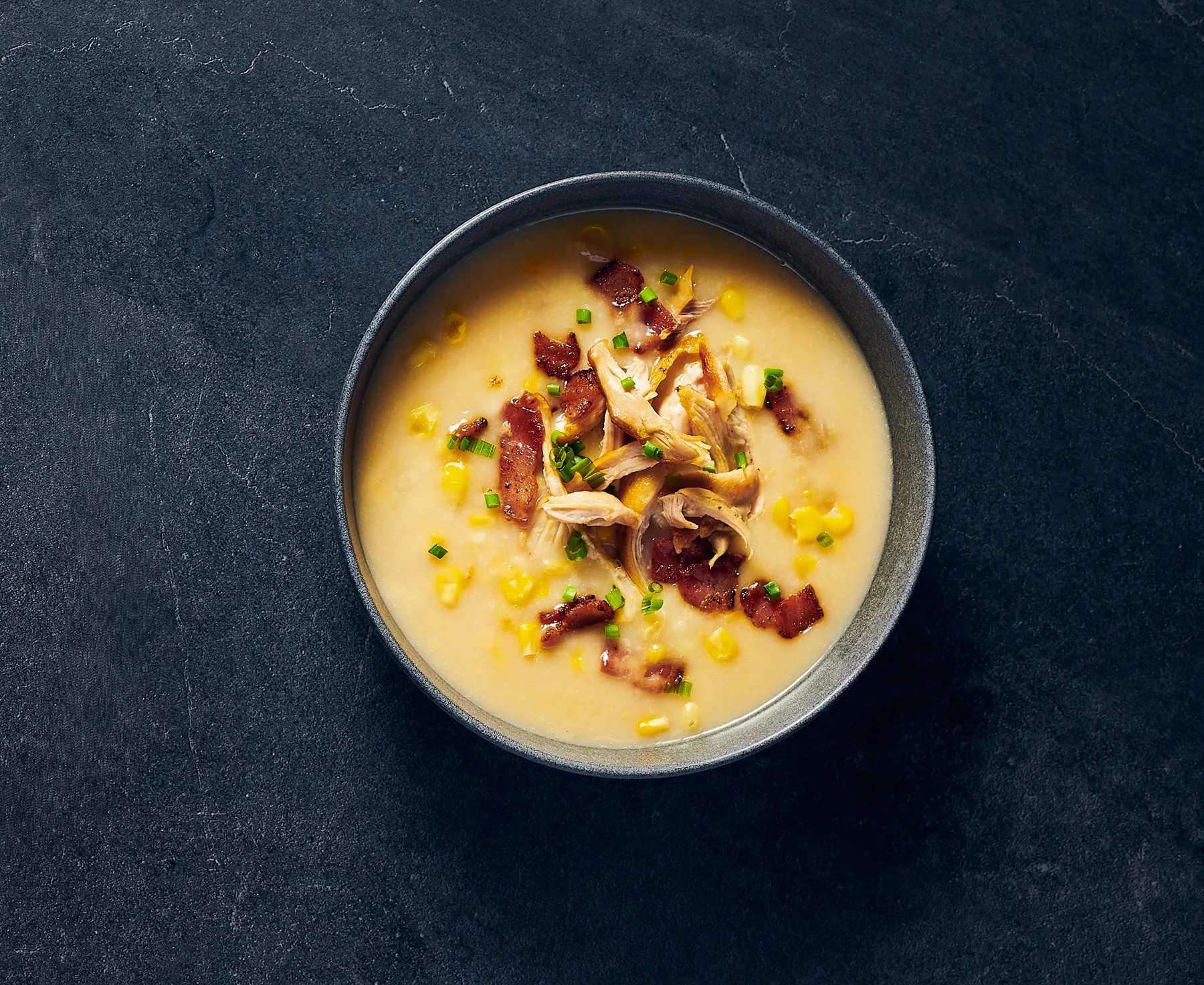 Bacon cheddar soup in black bowl with black background
