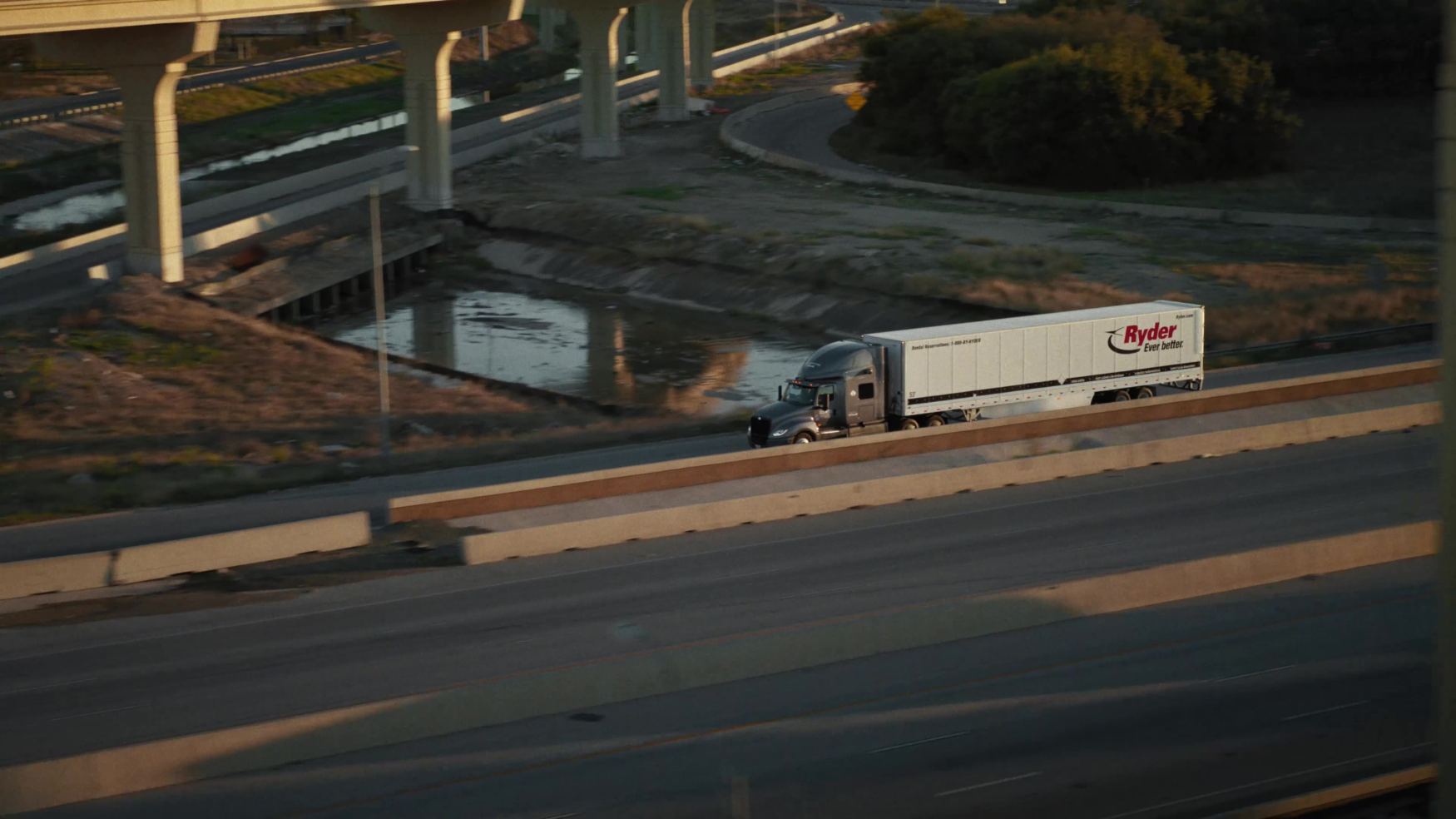 An aerial view of a Ryder semi-truck navigating a freeway interchange surrounded by overpasses and greenery