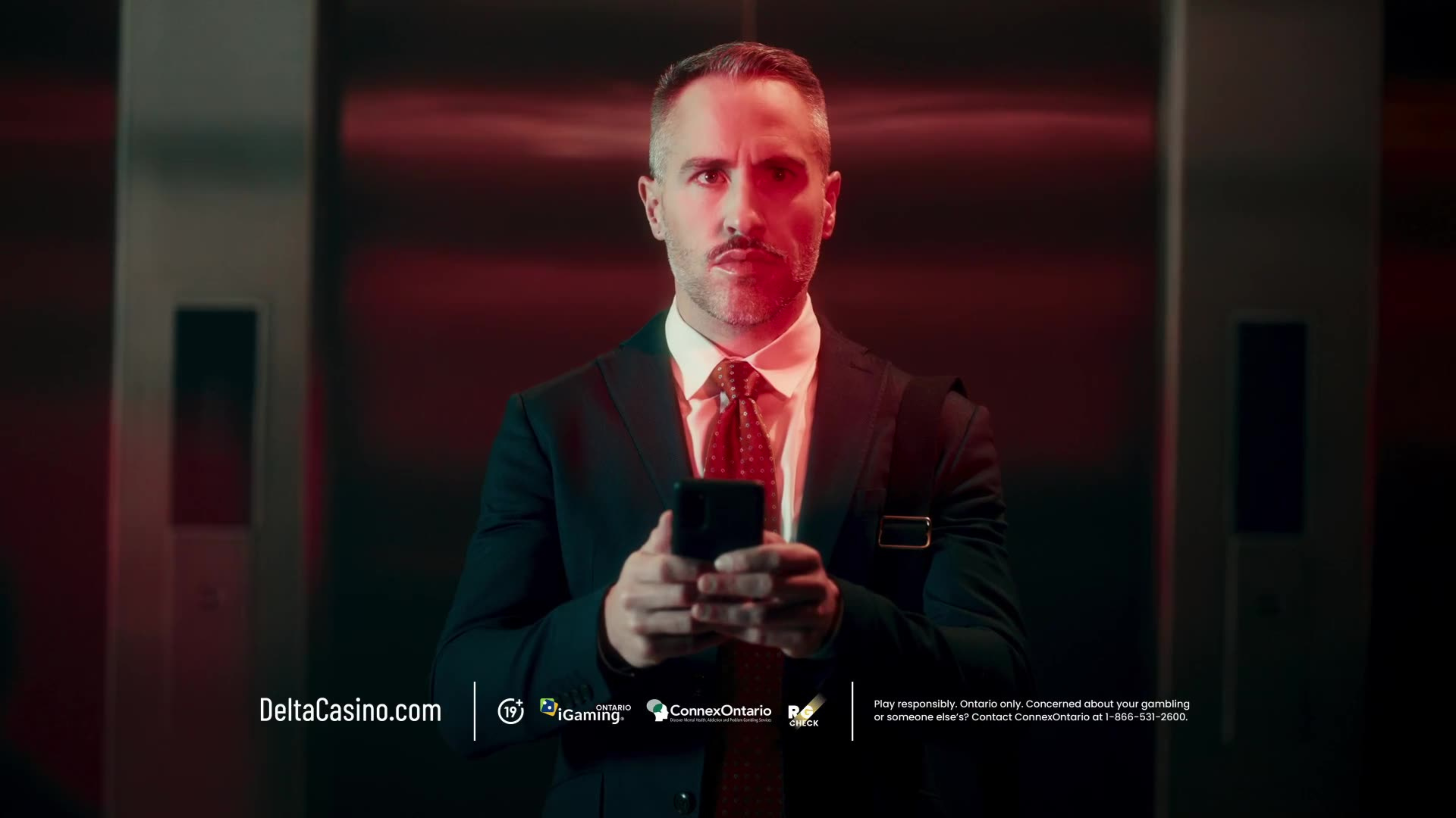 A sharp-dressed man in a suit holds a phone under dramatic red lighting in a Delta Casino ad.