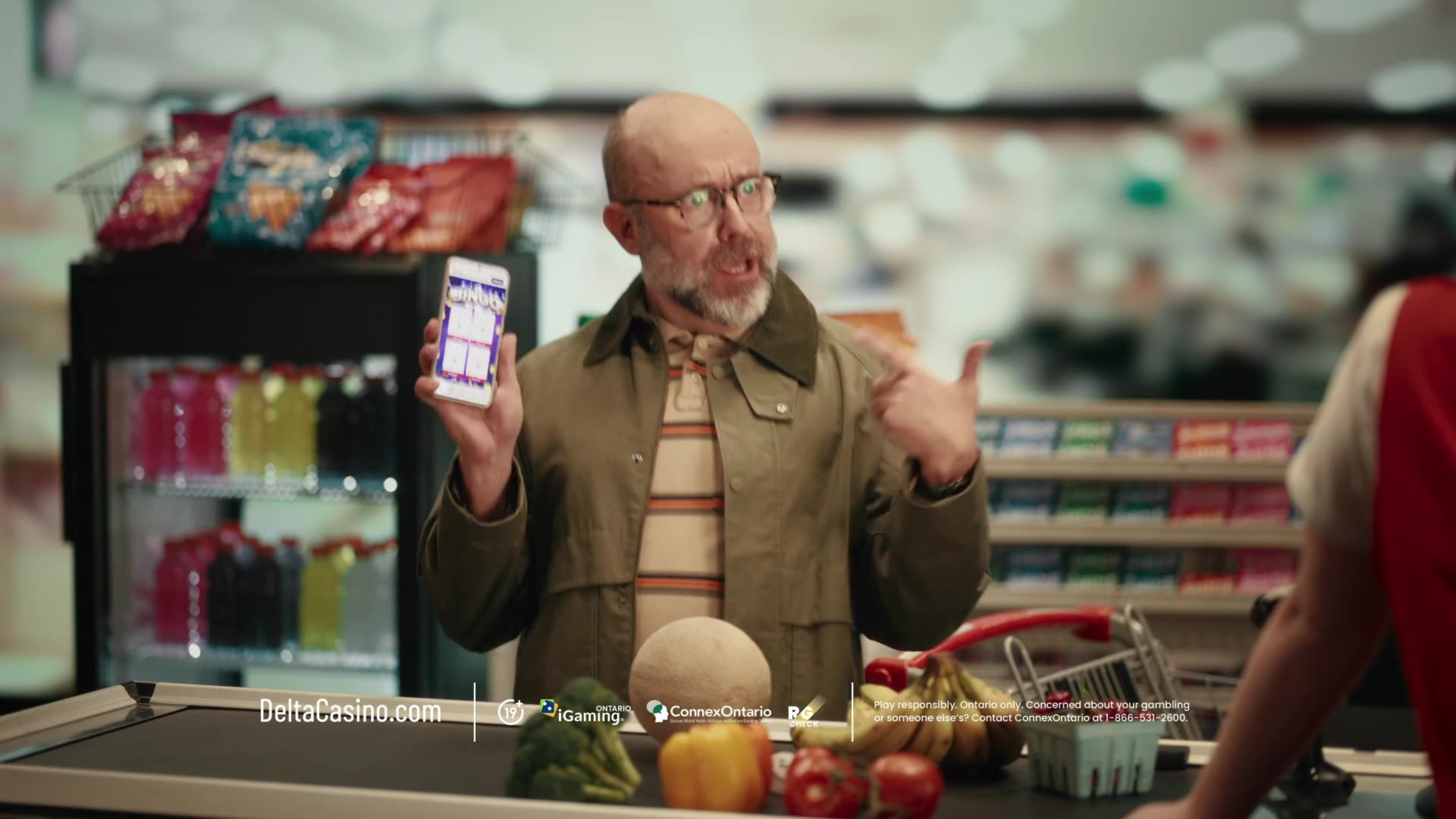 A bald man at a grocery store checkout holds up his phone showing a casino app in a Delta Casino ad.