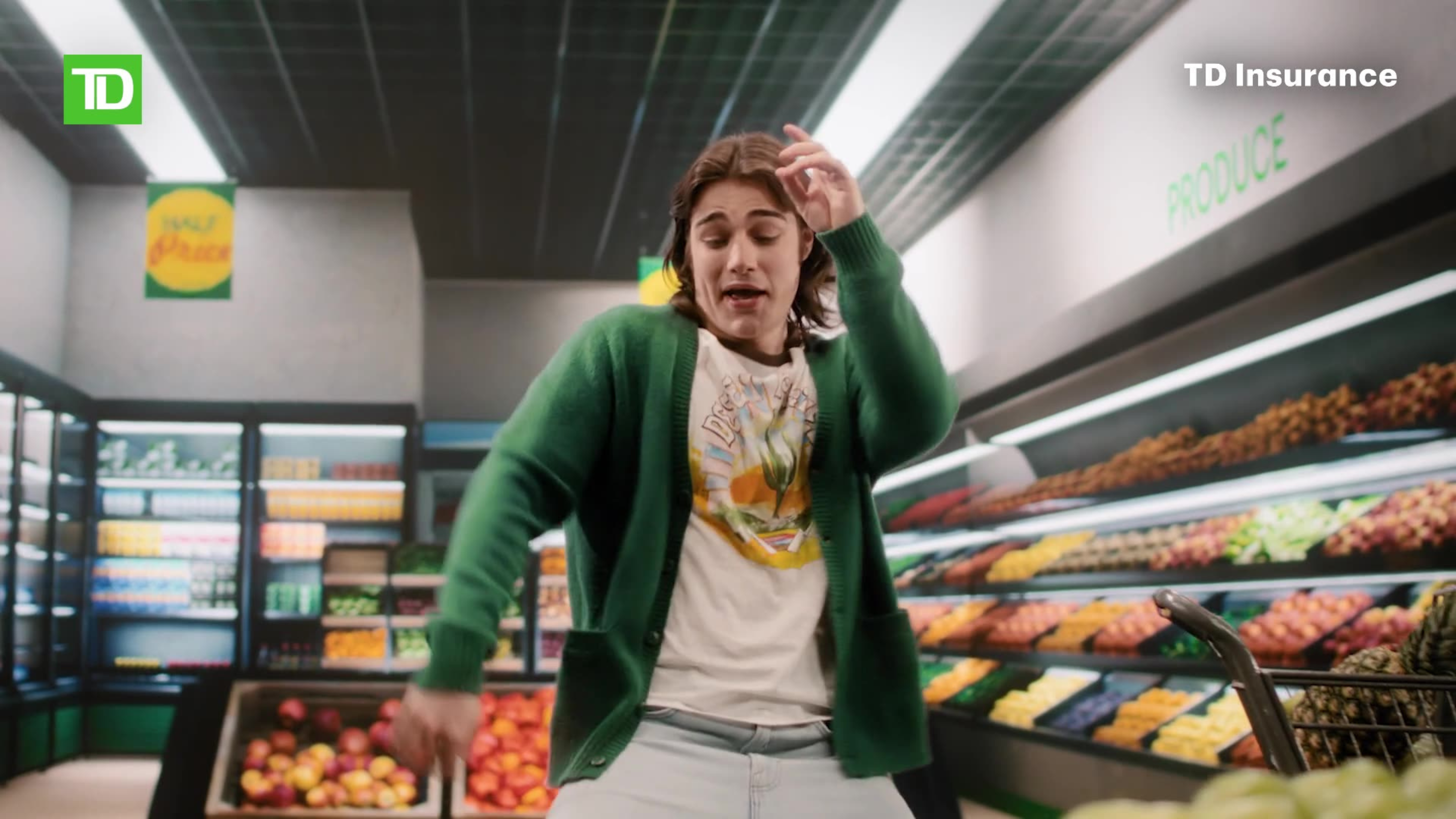 A woman in a green cardigan dances expressively in a grocery store produce aisle in a TD Insurance ad.