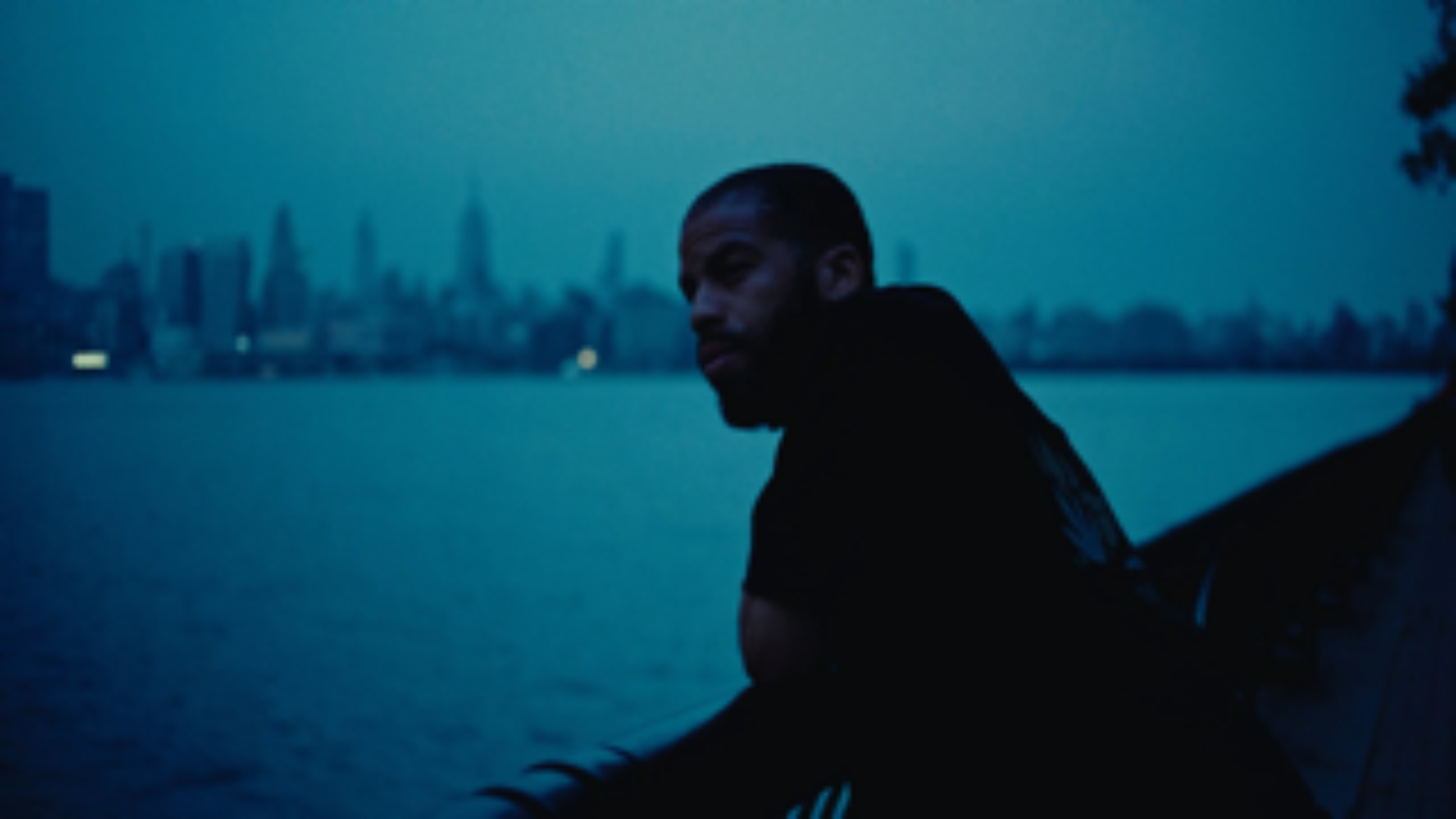 A man leans on a waterfront railing at dusk, reflecting over the city skyline.